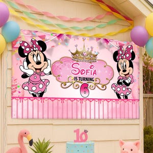 Op de afbeelding: Een roze banner met Minnie Mouse-illustraties, een kroon en de tekst "Sofia wordt 6". Minnie Mouse draagt een roze jurk met stippen en een strik. De banner is versierd met roze en gouden accenten en is omgeven door ballonnen en slingers.