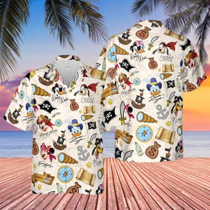 May include: Off-white short-sleeved button-down shirt featuring a pirate-themed pattern with Disney characters. The design includes pirate ships, treasure maps, compasses, and character illustrations of Mickey Mouse, Donald Duck, and Goofy.