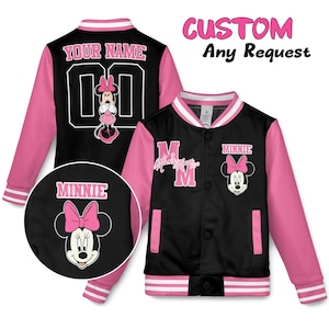 May include: Black and pink varsity jacket featuring Minnie Mouse. The jacket has pink sleeves, a white collar and cuffs, and a black body. The back of the jacket has the text "YOUR NAME" and the number "00". The front has the text "MINNIE".