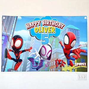 May include: A rectangular birthday banner featuring the text Happy Birthday Oliver 5 and Spidey and His Amazing Friends characters including Spider-Man, Ghost-Spider, and Spin against a city skyline background with blue and red colors.