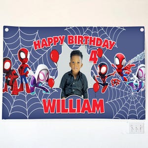 Puede incluir: Una pancarta de cumplea&ntilde;os rectangular azul con patrones de telara&ntilde;a blancos, texto rojo HAPPY BIRTHDAY y WILLIAM, el n&uacute;mero 4, globos rojos y personajes de ara&ntilde;as. Un recorte central muestra la fotograf&iacute;a de un ni&ntilde;o peque&ntilde;o.
