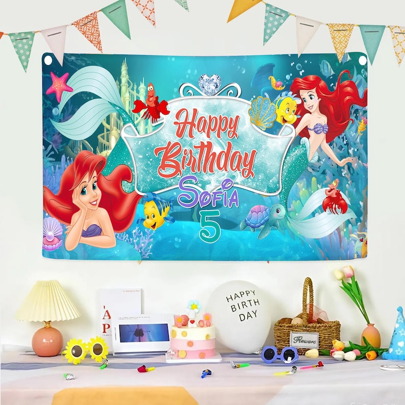 Puede incluir: Una pancarta de cumplea&ntilde;os rectangular con una escena submarina azul y personajes de La Sirenita, incluyendo a Ariel, Flounder y Sebasti&aacute;n. El centro muestra el texto Happy Birthday Sofia 5 en letras rojas y moradas.