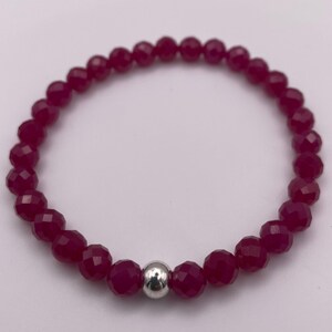 May include: A red gemstone bracelet with a silver bead accent. The bracelet is made of faceted beads and is approximately 7 inches in length.
