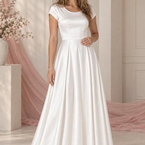 May include: A floor-length white satin dress featuring short sleeves, a round neckline, and a fitted bodice that transitions into a full, pleated skirt. The garment has a smooth, lustrous finish and a clean, structured silhouette throughout the design.