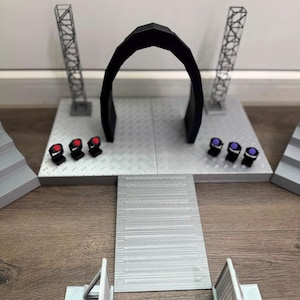 Può includere: Un set da palcoscenico in miniatura con una piattaforma argentata in lamiera mandorlata, un ingresso ad arco nero, due alte torri tralicciate verticali e sei piccole luci da palco con lenti rosse e viola. Una rampa argentata conduce alla piattaforma.