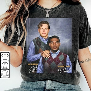 Op de afbeelding: Een antracietgrijs t-shirt met een grafische print van Joe Burrow en Ja'Marr Chase in argyle-truien over lichtblauwe overhemden. De tekst "JOE BURROW" en "JA'MARR CHASE" is afgedrukt samen met hun respectievelijke handtekeningen.