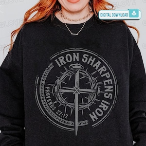 May include: Dark gray sweatshirt featuring a circular graphic with the text "IRON SHARPENS IRON" and "PROVERBS 27:17". The graphic includes a cross, a sword, and a crown of thorns. The words are in a distressed, vintage style.