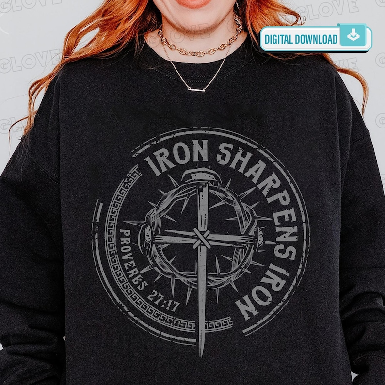 May include: Dark gray sweatshirt featuring a circular graphic with the text "IRON SHARPENS IRON" and "PROVERBS 27:17". The graphic includes a cross, a sword, and a crown of thorns. The words are in a distressed, vintage style.