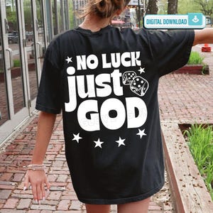 May include: A black short-sleeved t-shirt featuring white screen-printed text on the back that reads NO LUCK just GOD, accompanied by a graphic of two six-sided dice and several star shapes arranged around the bold lettering.