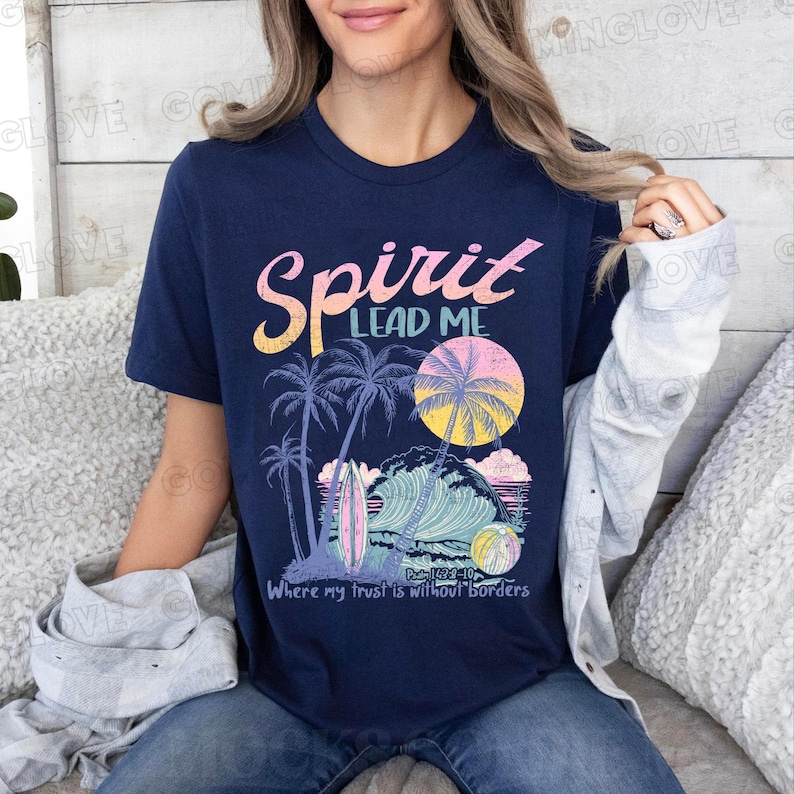 May include: A navy blue t-shirt with a vintage-style graphic of a beach scene with palm trees, waves, and a surfboard. The text "Spirit Lead Me" is printed in pink and white above the graphic, and the text "Where my trust is without borders" is printed below the graphic. The text "Psalm 62:10" is printed in small font below the graphic.