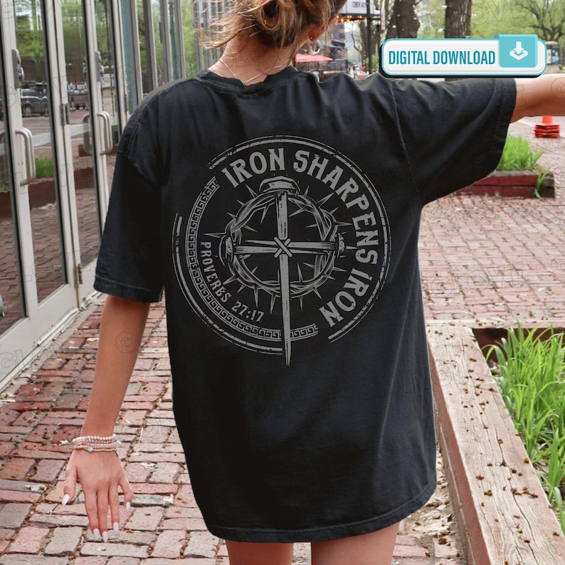 May include: Black t-shirt with a circular graphic on the back. The graphic features a cross, a crown of thorns, and the text "IRON SHARPENS IRON" and "PROVERBS 27:17". The shirt has short sleeves and a relaxed fit.