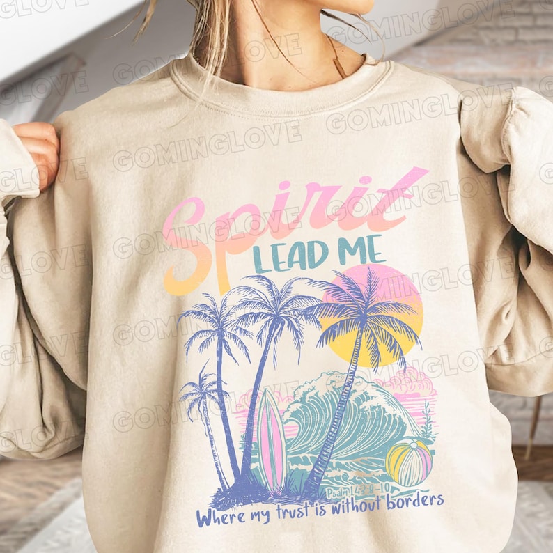 May include: A beige sweatshirt with a graphic design of palm trees, waves, and a sunset. The text "Spirit Lead Me" is in pink and blue lettering. The text "Where my trust is without borders" is at the bottom of the design. The scripture reference "Psalm 114:2-10" is also included.