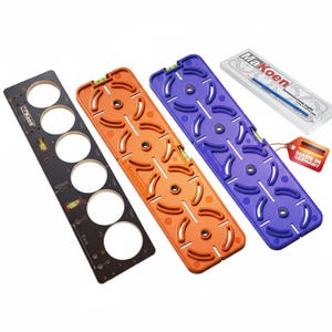 May include: Three colorful MaKoen tools: black, orange, and purple. Each tool has circular cutouts and a level. A clear case with a blue tool and a tag that says "Made in Germany" are also visible. The tools are designed for precise measurements.