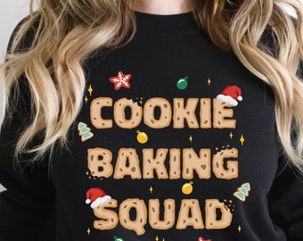 May include: Black sweatshirt with a Christmas cookie-themed design. The text reads "Cookie Baking Squad" with cookie-shaped letters and festive decorations.