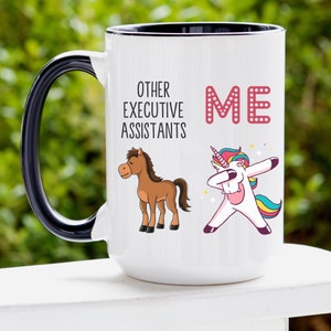 Op de afbeelding: Een witte keramische mok met een zwarte handgreep. De mok heeft een afbeelding van een eenhoorn die de "dab" doet en een bruin paard. De tekst op de mok luidt "Other Executive Assistants ME".