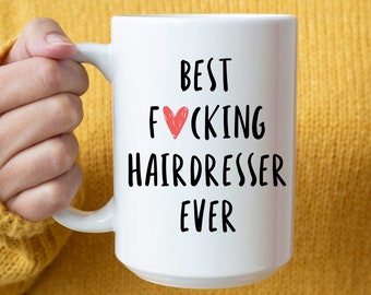 Peut inclure: Une tasse en céramique blanche avec un motif noir et rouge qui dit "Best F*cking Hairdresser Ever".