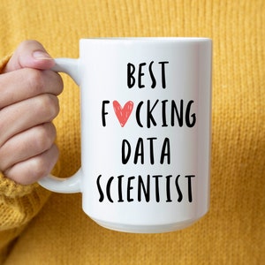 以下が含まれることがあります： 「BEST F*CKING DATA SCIENTIST」の黒い文字と「F*CKING」の「O」を赤色のハートで置き換えた白いセラミックマグ。マグカップには大きなハンドルがあり、黄色の背景に配置されています。