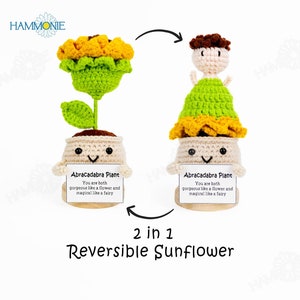 May include: A reversible crochet sunflower toy with a smiling face. One side features a sunflower with green leaves and a yellow center. The other side features a crocheted doll with a green dress and brown hair. Both sides are attached to a beige pot with a wooden base. The base has a label that reads "Abracadabra Plant. You are both gorgeous like a flower and magical like a fairy."