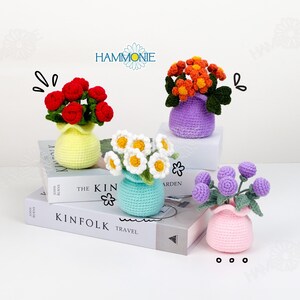 May include: Four crocheted flower arrangements in small vases. The flowers are red roses, orange blooms, white daisies, and purple buds. The vases are yellow, purple, turquoise, and pink. The word "HAMMONIE" is in the image.