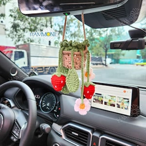 Peut inclure: Un charme de voiture en crochet en forme de fraise et de fleur suspendu à un rétroviseur. Le charme présente un pot en crochet rose et brun avec des feuilles vertes et trois fraises rouges. Le charme comprend également une fleur blanche en crochet avec un centre jaune.