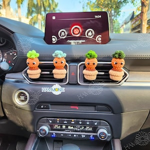 May include: Four crocheted car air fresheners shaped like potted plants. Each plant has a green top and a brown base. The air fresheners are hanging from the air vent of a car.