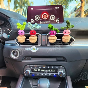 May include: Four crocheted radish air fresheners in a car. The radishes are pink, red, green, and purple. They are hanging from the air vents in the car.
