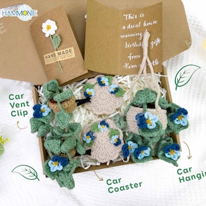 May include: A gift box filled with handmade crocheted items, including a car vent clip, a car coaster, and a car hanging ornament. The items are decorated with green leaves and blue flowers. The box also includes a card that says "This is a dual house warming birthday gift from Kem"