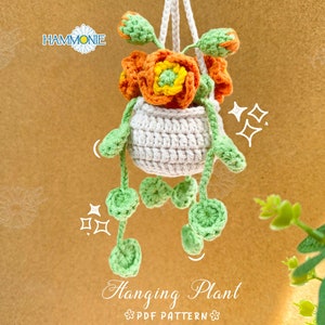 May include: A handmade crochet hanging plant featuring orange and yellow flowers in a white pot. The plant has green leaves and is suspended by a white cord. The text "Hanging Plant PDF Pattern" is visible.