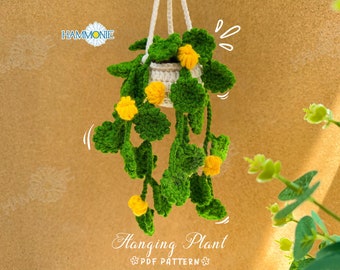 May include: A crocheted hanging plant with green leaves and yellow flowers in a white pot. The plant is hanging from a white string. The background is a brown textured surface. The text "Hanging Plant PDF PATTERN" is at the bottom of the image.