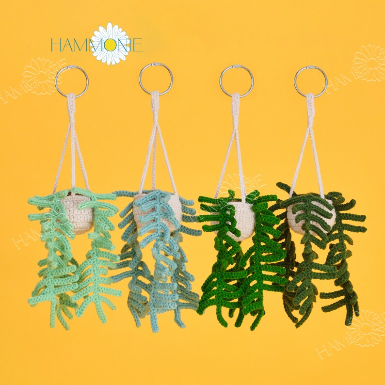 May include: Four crocheted hanging plant pots with green and white leaves. The pots are attached to silver rings and white cords.