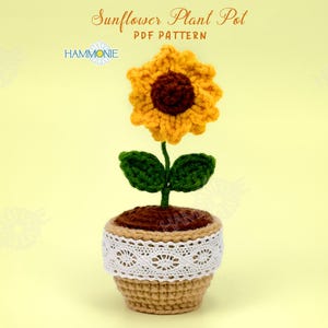 May include: Crocheted sunflower plant pot with a brown center, yellow petals, green leaves, and a brown pot with white lace trim. The pot is sitting on a yellow background. The text "Sunflower Plant Pot PDF Pattern" is above the image.