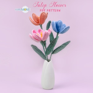 May include: A crocheted bouquet of three tulips in a white vase. The tulips are pink, blue, and orange. The vase is shaped like a tulip.