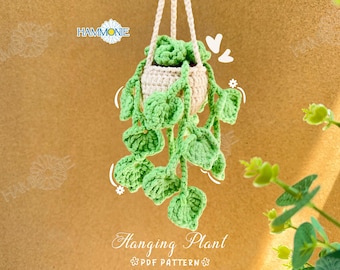 May include: A crocheted hanging plant with green leaves and a beige pot. The plant is hanging from a white string and the background is a brown textured surface. The text "Hanging Plant PDF Pattern" is at the bottom of the image.