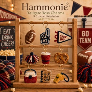 May include: Nine crochet keychains hanging on a wooden rack, featuring shapes like a football, foam finger, pennant with text GAME DAY, pom-pom, cup, pretzel, cooler, play chart, and whistle. The text Hammonie Tailgate Toss Charms 9 Crochet Keychains is visible.