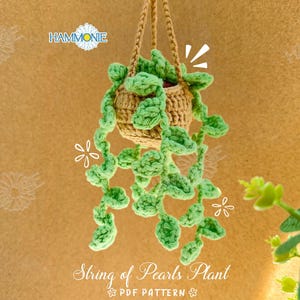 May include: A handmade crochet String of Pearls plant in a hanging basket. The plant features light green, pearl-shaped leaves cascading from a tan-colored basket. The basket is suspended by a braided tan cord. The text "String of Pearls Plant" is visible.