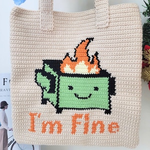 May include: A beige crocheted tote bag featuring a green, black, and orange pixelated image of a burning bin with a smiling face. The text "I'm Fine" is written in orange below the image.