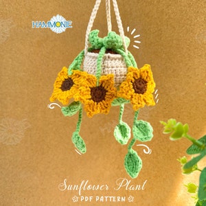 Könnte beinhalten: Eine gehäkelte Sonnenblumenpflanze, die an einem Makramee-Hänger hängt. Die Pflanze hat drei gelbe Sonnenblumen mit braunen Zentren und grünen Blättern. Der Text "Sunflower Plant PDF Pattern" befindet sich am unteren Rand des Bildes.