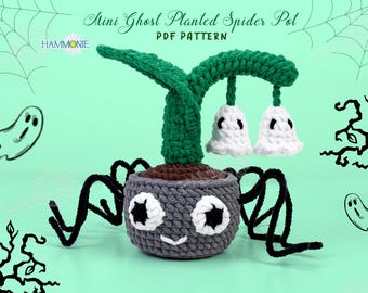 May include: A crocheted spider pot with a green plant and two white ghost-shaped flowers. The pot has a gray and brown color scheme and a cute face with black eyes and a white smile. The spider pot is sitting on a light green surface.  Mini Ghost Planted Spider Pot PDF Pattern.