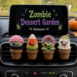 May include: Four small crocheted figures in brown pots attached to a car air vent. The figures include a pink-topped cupcake, a candy corn, a donut, and a ghost. A car screen displays the text Zombie Dessert Garden and Hammonie.