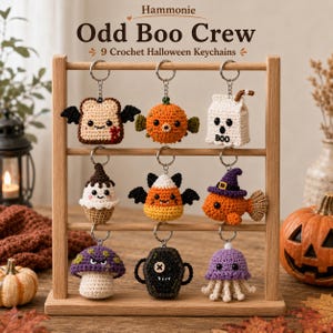 May include: Nine crochet Halloween keychains hanging on a wooden rack, labeled Odd Boo Crew. The figures include a bat-winged toast, a pufferfish, a milk carton, a cupcake, a candy corn bat, a fish in a witch hat, a mushroom, a coffin, and a jellyfish.