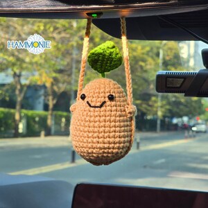 May include: A crocheted car charm shaped like a smiling potato with a green leaf on top, hanging from the rearview mirror. The charm is tan with black eyes and a stitched smile. The word "HAMMONIE" is visible.