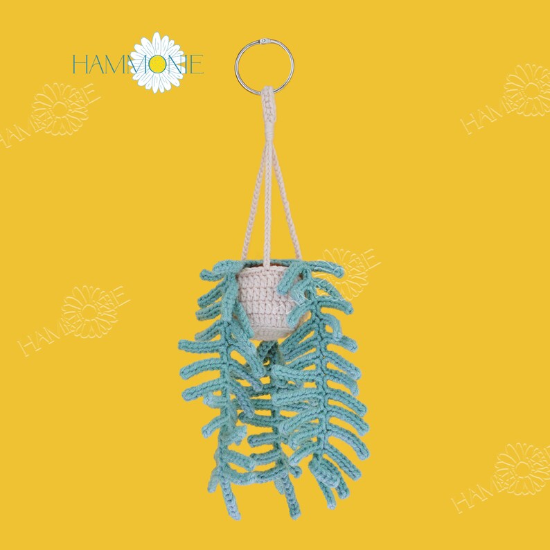 May include: A crocheted hanging planter with a light brown pot and green leafy vines. The planter is hanging from a silver ring.