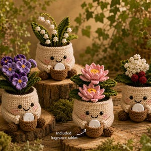 May include: Four crocheted plant pots with smiling faces, each holding a small brown basket containing a white fragrance tablet. The plants include lily of the valley, purple pansies, pink lotus flowers, and white blossoms with red berries.
