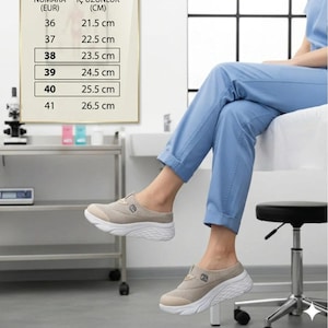 Op de afbeelding: Beige instappers met een witte zool. De schoenen worden getoond op een persoon die een lichtblauwe broek draagt. Een tabel toont schoenmaten in EUR en de bijbehorende binnenlengte in cm.
