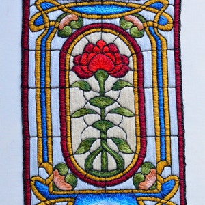 May include: Embroidered artwork depicting a red rose in a stained glass style frame. The frame is made up of black, red, blue, yellow, and green thread.