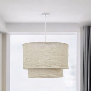 Puede incluir: Una lámpara colgante blanca con una pantalla de lino de doble capa. La pantalla es de color beige claro y tiene un tejido texturizado.