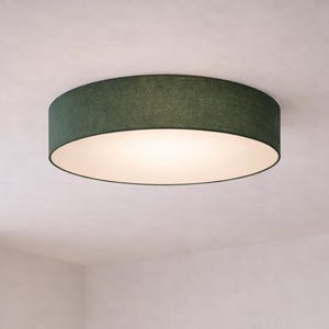 Könnte beinhalten: Runde Deckenleuchte in Dunkelgrün mit weißem Innenraum. Die Leuchte ist an einer weißen Decke montiert und beleuchtet den Raum. Die Leuchte hat eine stoffartige Textur.