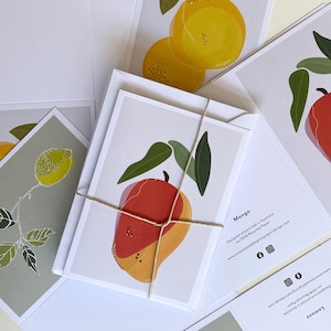 May include: A set of greeting cards featuring illustrations of a mango and lemons. The cards are designed and printed in Australia on 100% recycled paper. The text on the cards reads "Mango" and "Lemons".