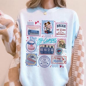 May include: A light blue crewneck sweatshirt featuring a collage of Off Campus themed graphics, including a keyboard, hockey players, Briar University text, a stack of books, and various stamps with red and blue accents on the front center.