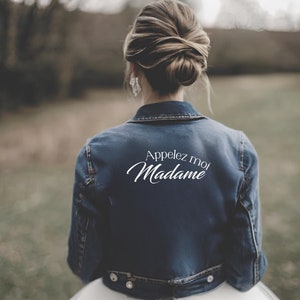 Peut inclure: Une femme portant une veste en jean bleue avec le texte "Appelez moi Madame" en lettres blanches au dos.